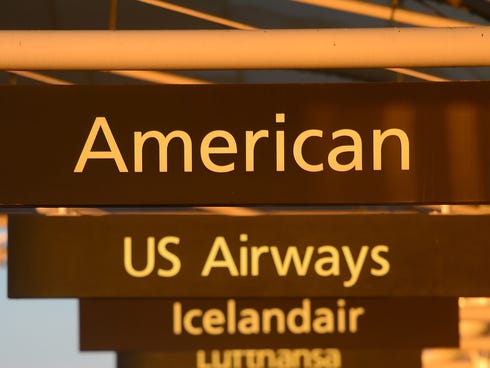 American Airlines and US Airways signs stand next to each others at Denver International Airport. The two airlines have merged and announced new customer benefits.