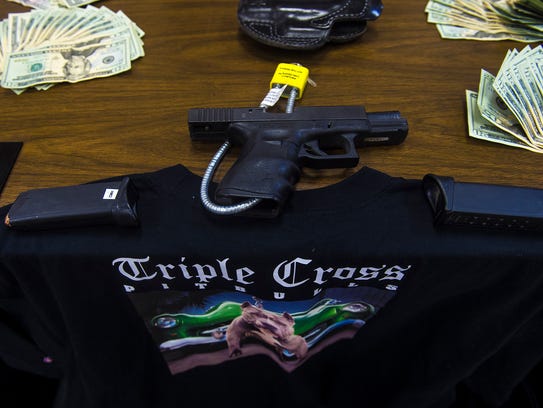 A gun, bills and a shirt displaying a Triple Cross