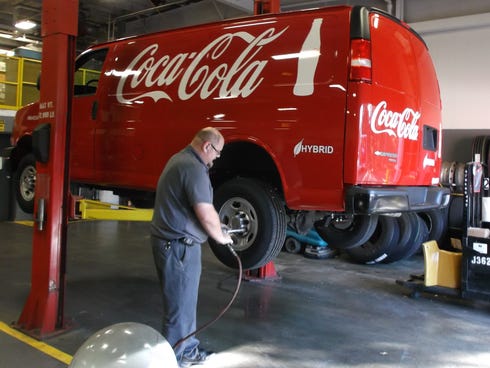 A worker attends to a wheel on one of the vans that Coke is converting to hybrid power