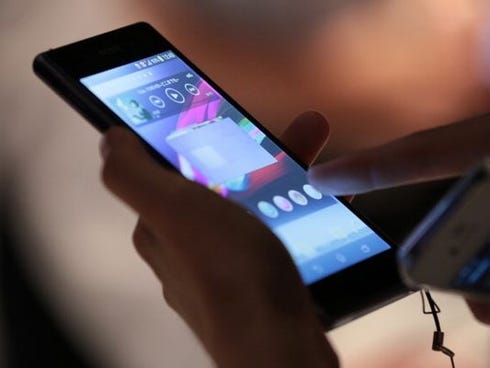 A member of the media, holding Apple Inc's iPhone 4, right, tries out a Sony Corp. Xperia Z1 smartphone after a news conference in Tokyo, Japan, on Friday, Sept. 13, 2013. Sony Corp. is betting its Xperia Z1 handset will propel it to No. 3 in the sma