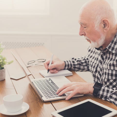 Older man typing on laptop while writing on a note