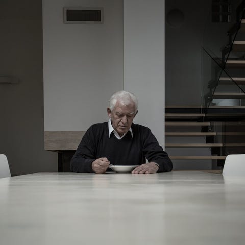 Older man eating alone at table in house.