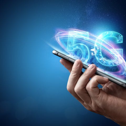 A hand holding a mobile device with 5G written abo