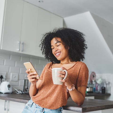 A person smiles and looks at a phone in a kitchen.