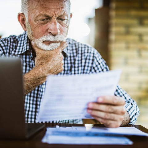 An older person at a laptop studying a document.