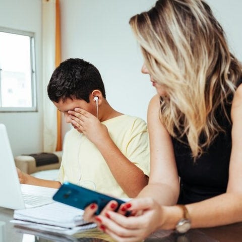 A mom sitting next to her son while he does homewo