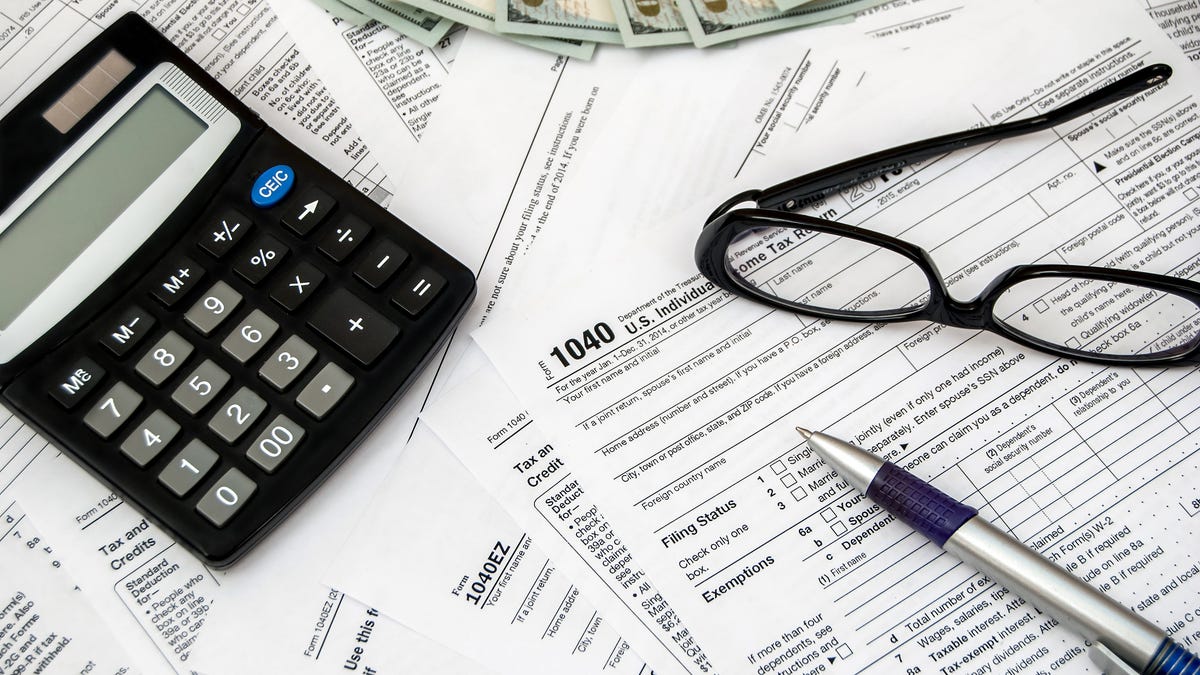 Tax forms, pen, glasses, calculator, and money on a flat surface.