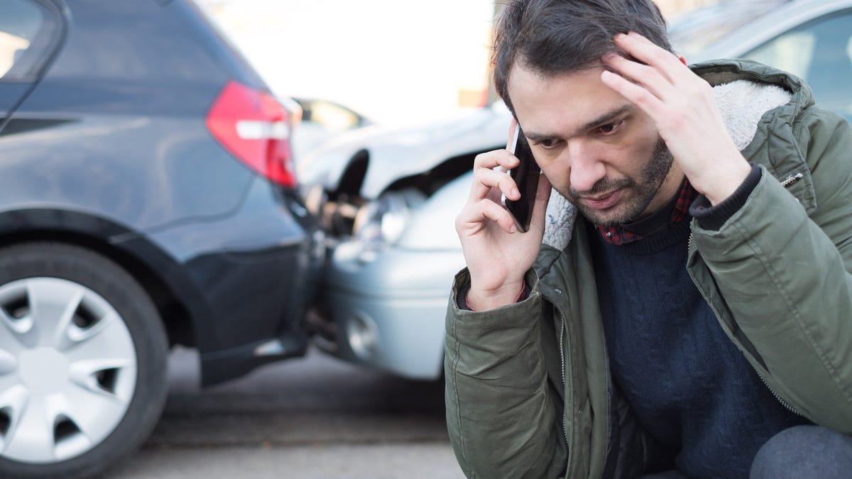 Person on the phone in front of  two cars with damage.