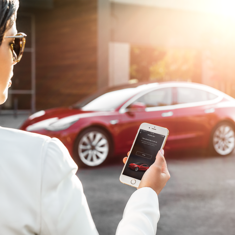 A woman unlocks a Model 3 with a Tesla app on her...