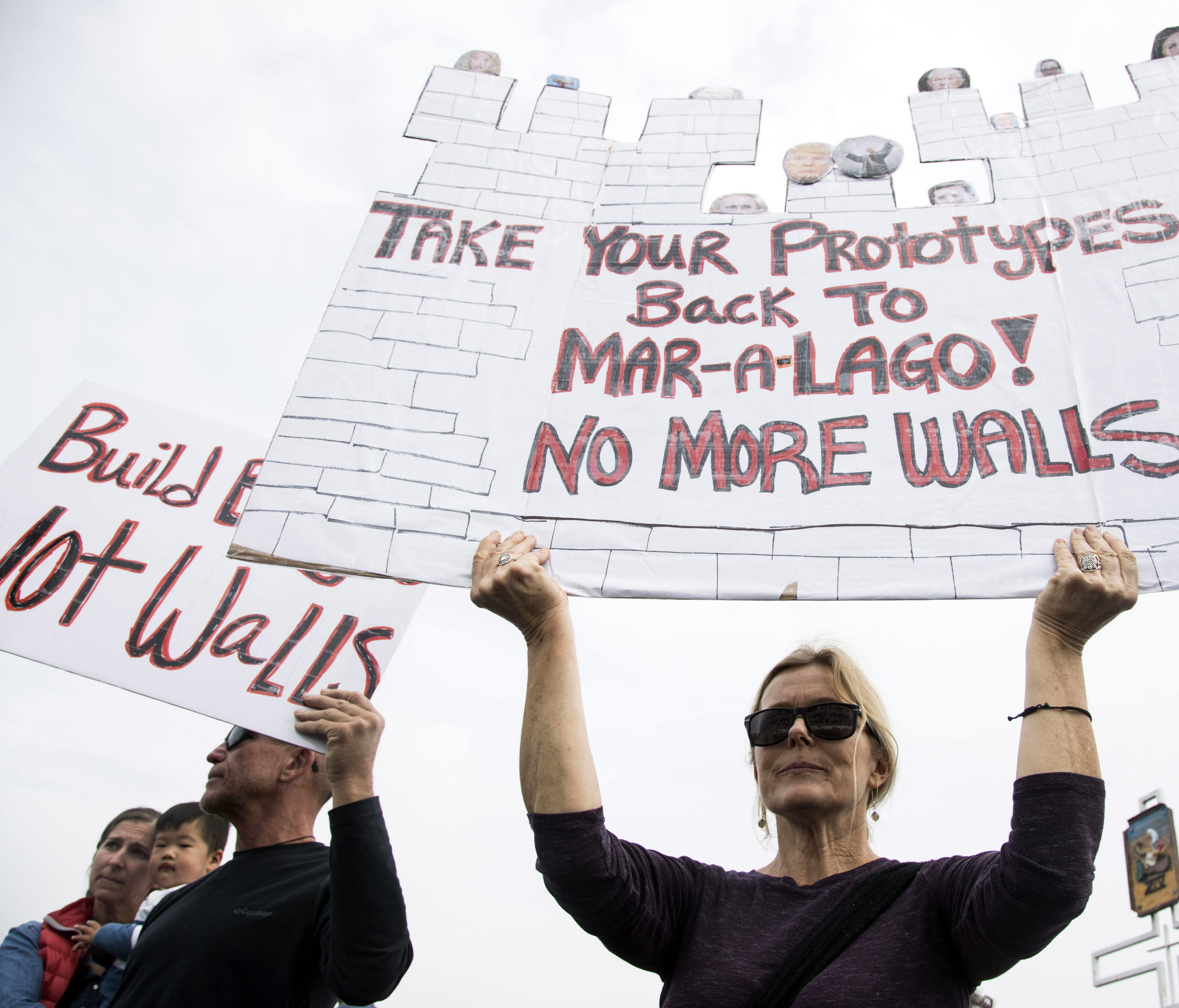 Bill Sparks, left, holds a sign with Sarah Garfield as hundreds of protesters gather outside Our Lady of Mount Carmel Catholic Church in San Ysidro,, Calif. to protest during President Trump's visit to see border wall prototypes.