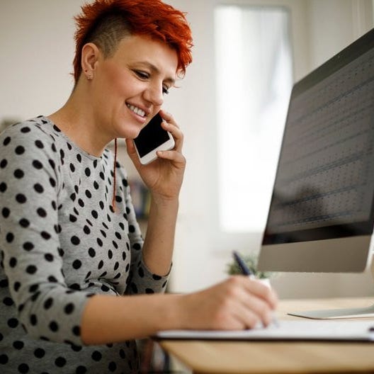 Woman working from home using computer, phone, and laptop.