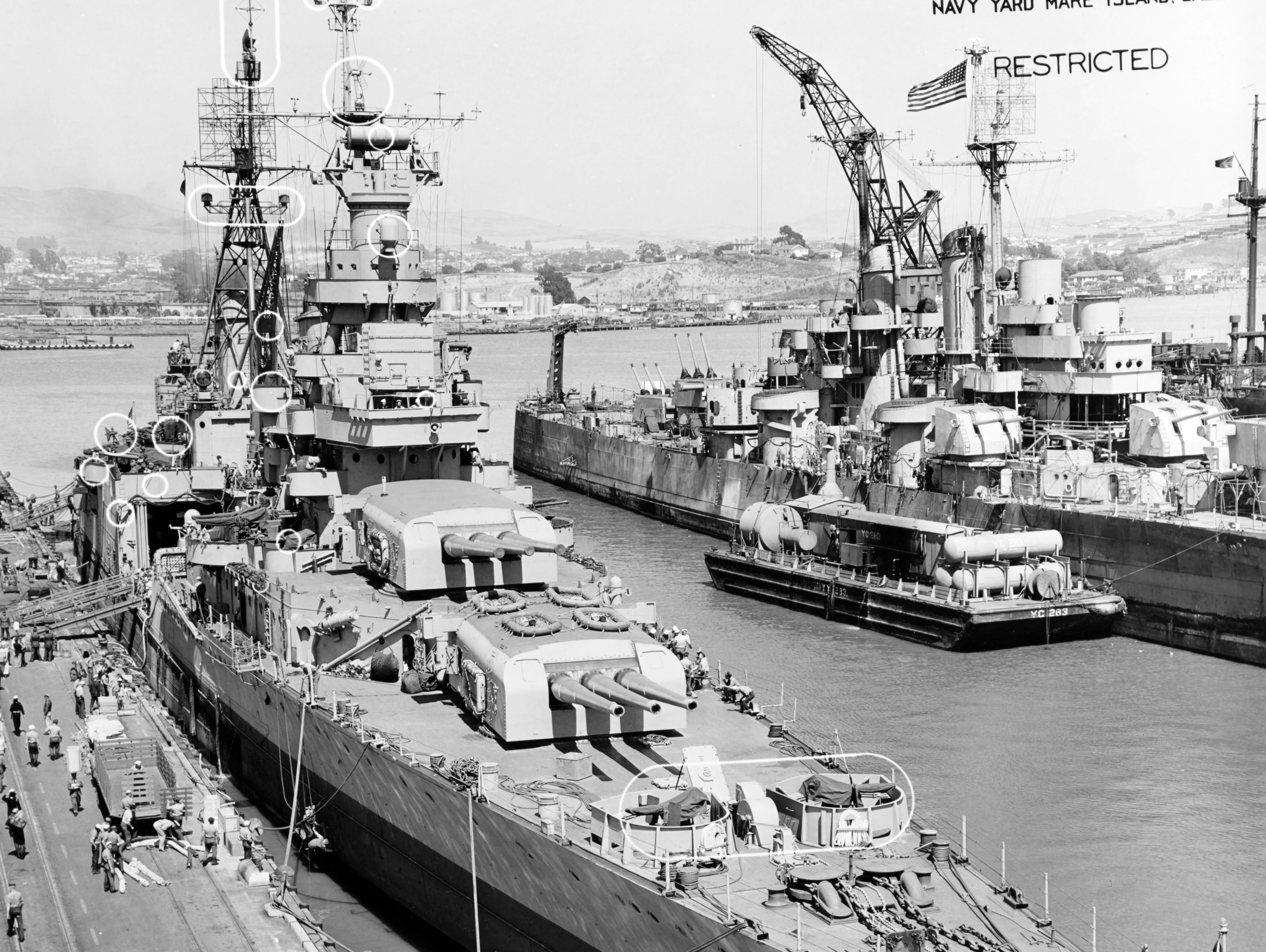 At the Mare Island Navy Yard after her final overhaul, July 12, 1945. Circles on photo mark recent alterations to the ship. Note stripped Cleveland class light cruiser in the right background, with YC-283 alongside.