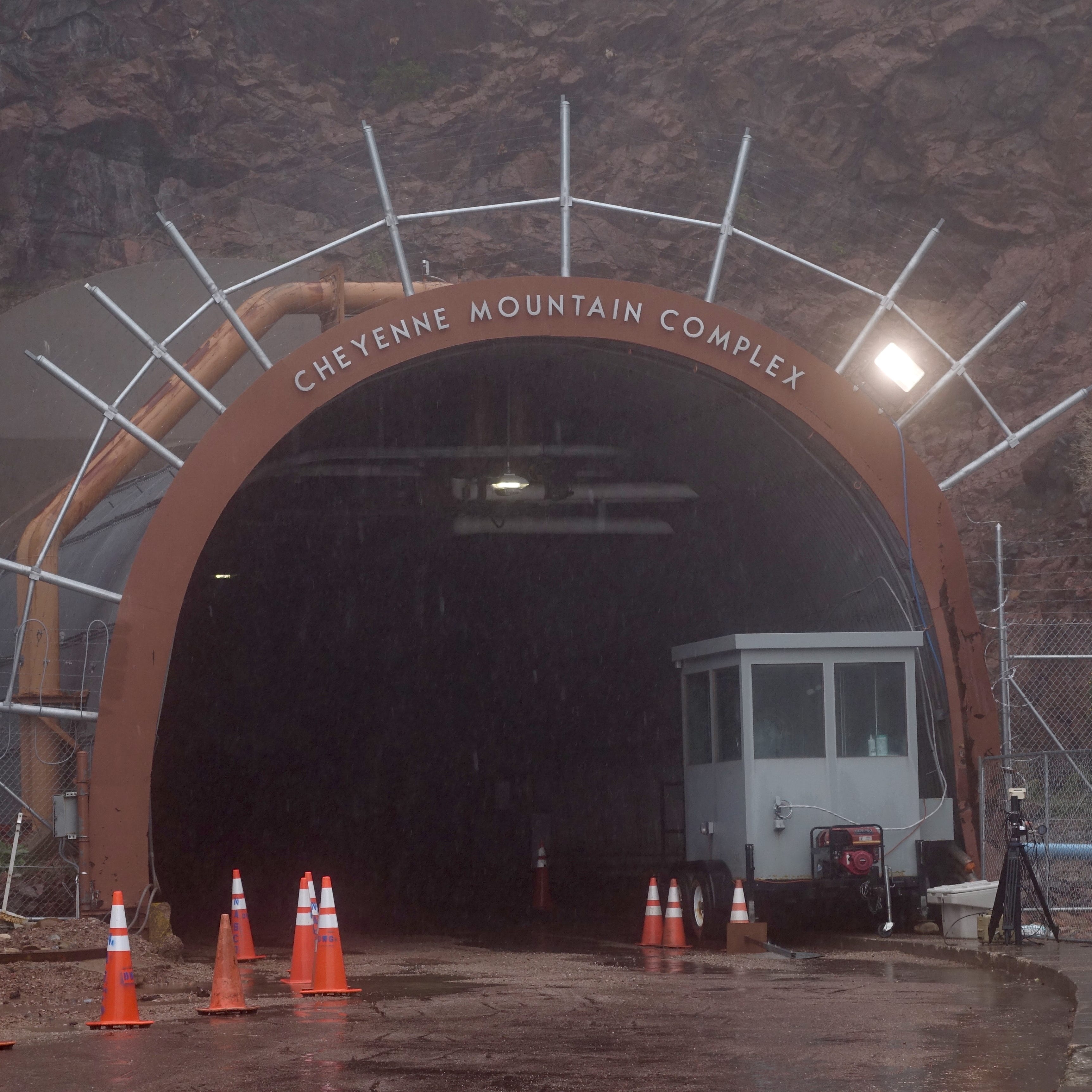 Rain falls in front of the iconic entrance to the Cheyenne Mountain bunker beneath a Colorado mountain. The tunnel travels a mile through solid rock before reaching the blast doors behind which the bunker sits. Heavy security measures restrict photography of the site.