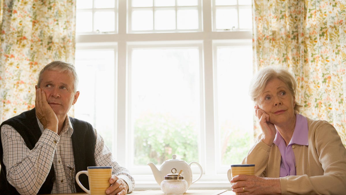 Older man and woman sitting at a table, looking worried