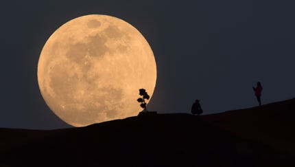 TOPSHOT - A person poses for a photo as the moon...