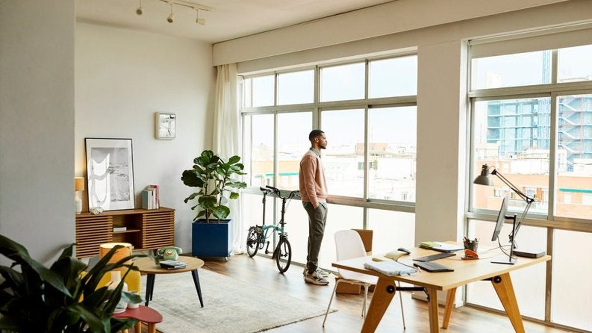 A person standing and looking out the window of their apartment.