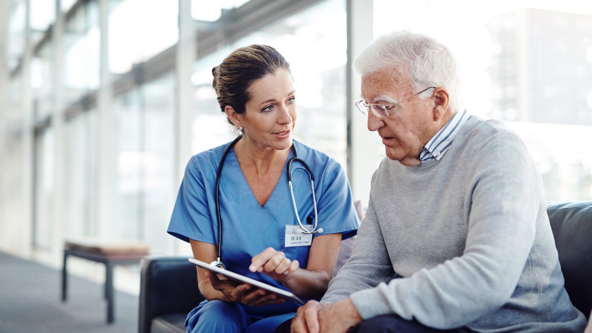 A person in scrubs talking to a seated person.