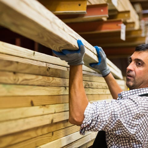 Person picking up lumber off the shelf at store.