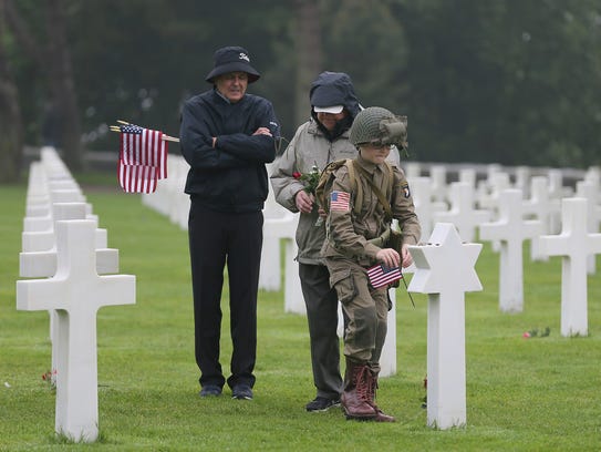 David Chamberlain, left, grandfather Charly Powers and his son Steve, from Atlanta, pay their respect by placing a U.S. flag on the grave of a U.S. soldier who died during World War II at the Colleville American military cemetery in France on June 6, 2018, the 74th anniversary of the D-Day landing.