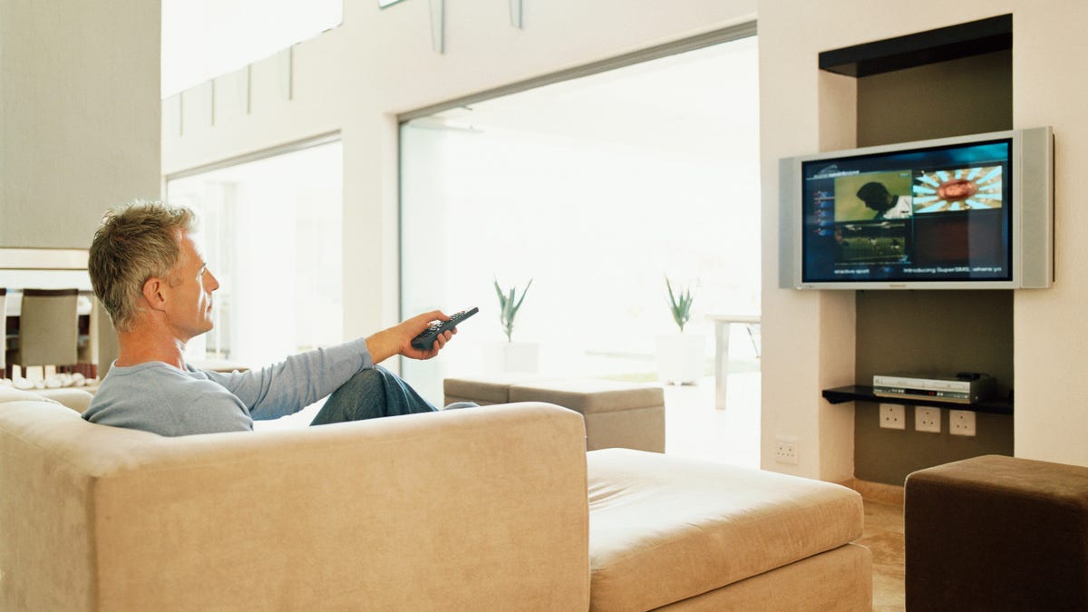 A man on a couch pointing a remote at a television.