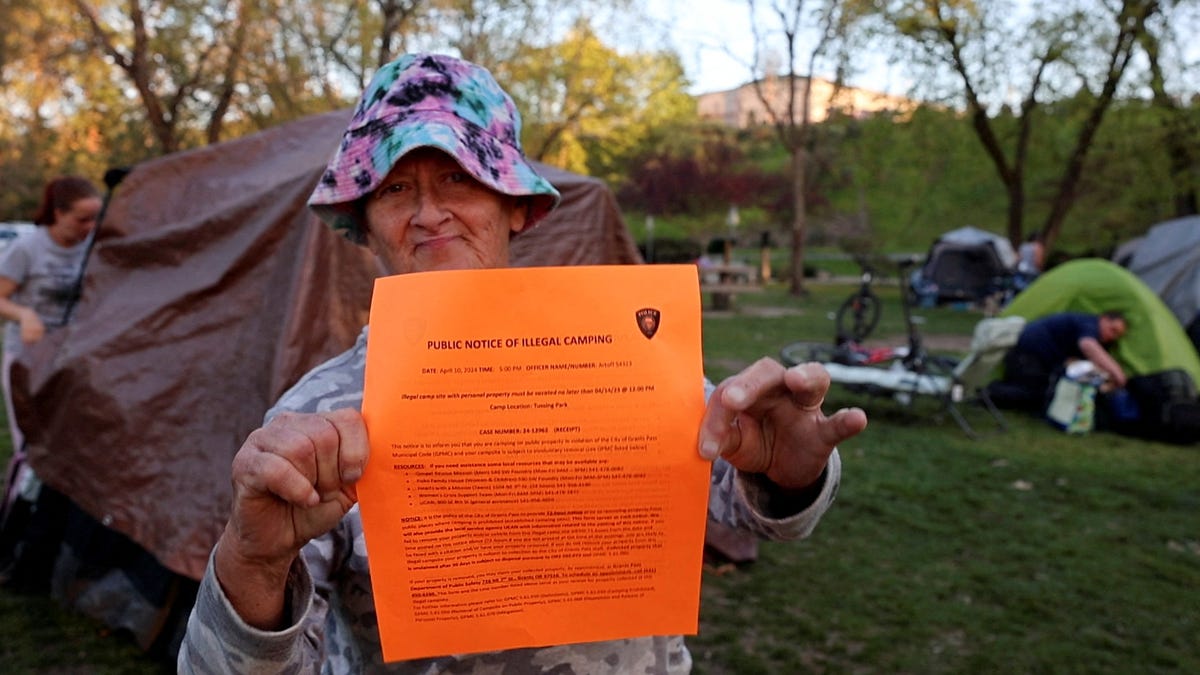 An unhoused woman named Kimberly Morris holds up a notice a police officer gave her giving her 72 hours to move her tent from the park, in Grants Pass, Oregon, U.S, April 18, 2024. REUTERS/Deborah Bloom