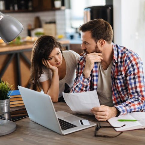 A worried couple looks at bills, with a laptop and a credit card on the table.