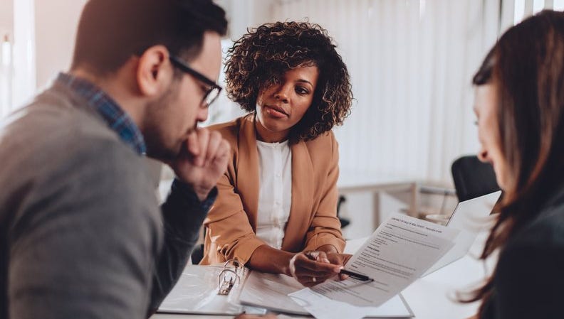 A couple decides whether to sign a mortgage agreement or not while sitting at a desk in a bank.