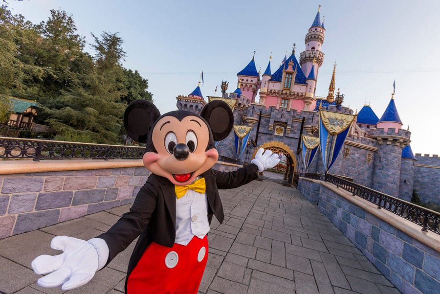 Mickey Mouse stands in front of the Sleeping Beauty Castle to welcome fans back to Disneyland.