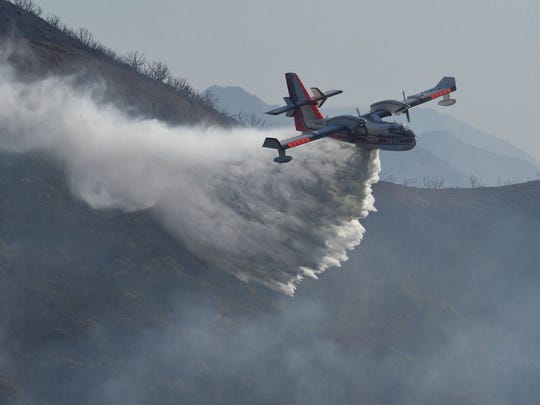 On this archival photo provided by the Santa Barbara County Fire Department, a Bombardier 415 Super Scooper is throwing a drop of water on hot spots along the hill at L & B. is Gibraltar Road in Santa Barbara, California on Sunday morning December 17, 2017. According to the US Forest Service, Scooper aircraft stationed in Chico are available to fight the Hirz fire near Shasta Lake, once the smoke is dissipated