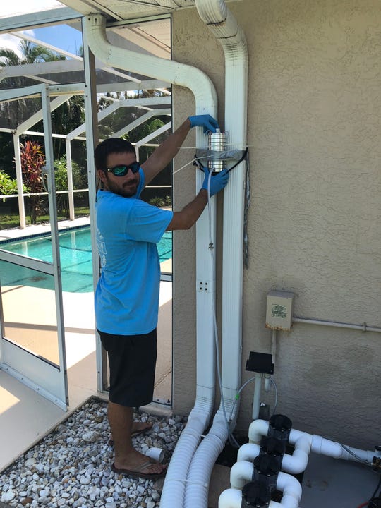 Adam Catasus, a graduate student at Florida Gulf Coast University, is installing an algae-based air sampling pump outside a Cape Coral home.