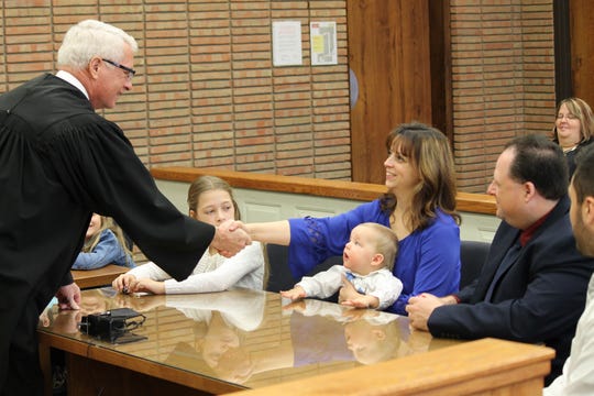 Nikki Stromberg shakes hands with Judge Elwood Brown during adoption proceedings in Port Huron as her husband, Reid, watches. She holds her foster son, David, as his new big sister Beth watches proceedings on Jan. 15, 2016.