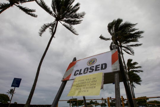   In this archival photo from August 8, 2014, winds from tropical storm Iselle blow palms near a warning sign of the closure of Kualoa Regional Park in Honolulu. A winter storm Sunday carried the wind to 54 km / h and waves up to 60 feet. 