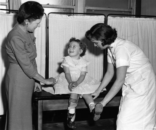 Eileen Connor of Waldwick, a three-year-old polio enthusiast, is very fond of her current treatments in Bergen Pines, administered by nurse Brenda Bellaviana, under the supervision of Northern District Campaign Chair Desiree Mittelstadet, Ridgewood. 14 JAN 1958