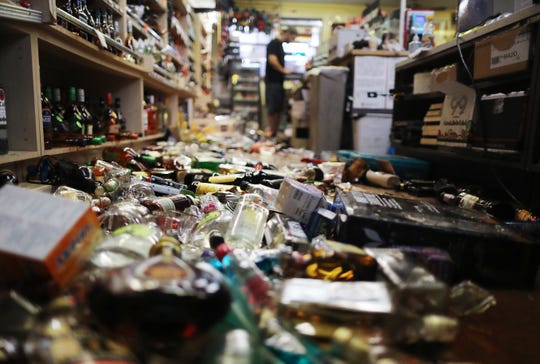 An employee is working at the checkout near broken bottles scattered on the ground, following a magnitude 7.1 earthquake that struck Friday in Ridgecrest, California.