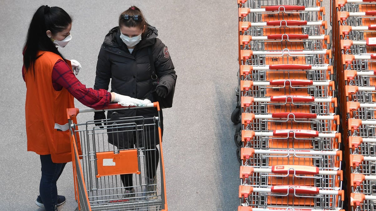 An employee wearing a protective face mask disinfects shopping carts for customers arriving to shop at a supermarket in Vienna, Austria on April 1, 2020, during the new coronavirus COVID-19 pandemic.  The Austrian government announced that shoppers in supermarkets will have to wear face masks in order to further clamp down on the spread of the novel coronavirus.