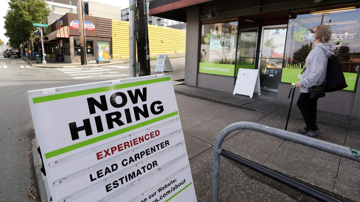 In this photo taken Thursday, June 4, 2020, a pedestrian wearing a mask walks past reader board advertising a job opening for a remodeling company, in Seattle.