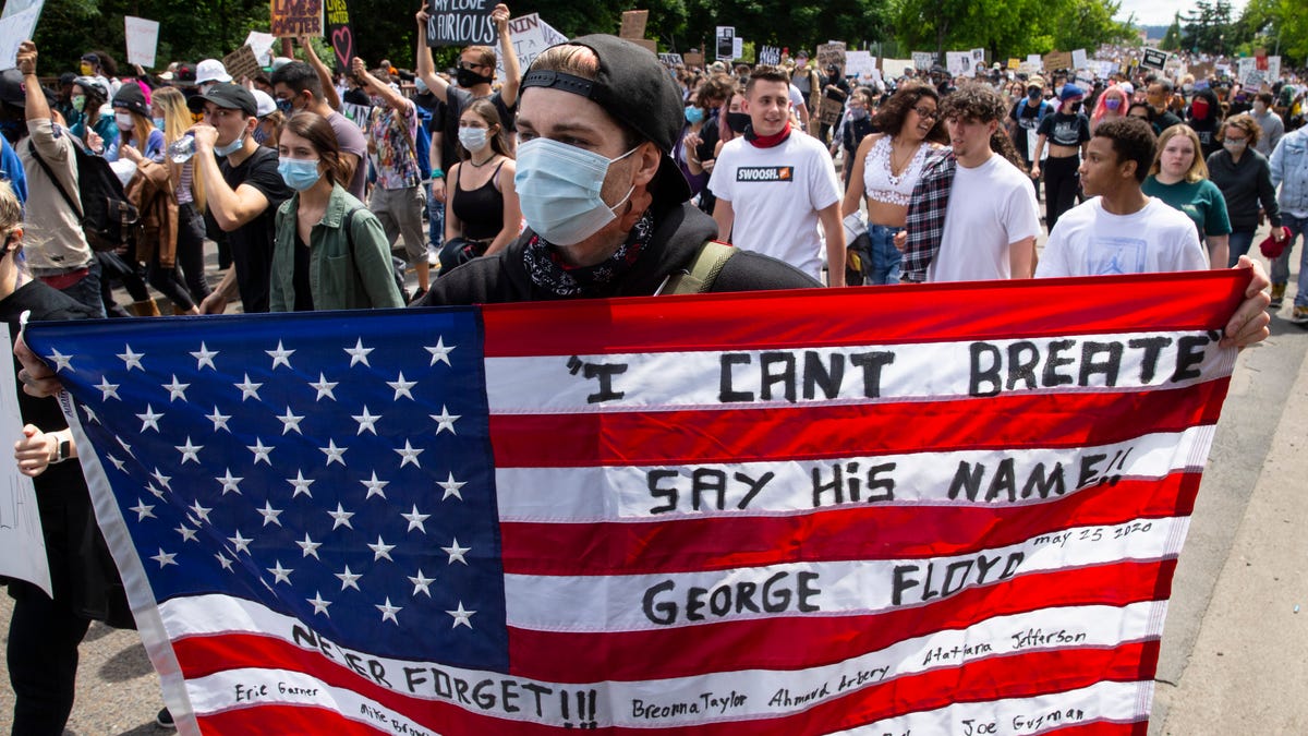 A young man wearing a face mask and holding an American flag joins the Black Lives Matter march in Eugene, Ore., May 31, 2020. Other protesters have held the flag upside down, a signal of distress.