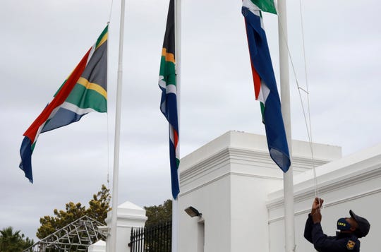 A policeman adjusts South African flags to half-mast outside parliament in Cape Town, South Africa, Wednesday, Nov. 25, 2020. South Africa declared five days of mourning starting today to remember those who have lost their lives to COVID-19 and gender-based violence.