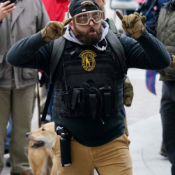 Roberto Minuta outside U.S. Capitol on Jan. 6, 2021, with military gear including hard-knuckle tactical gloves, ballistic goggles, a radio with an ear piece, and possibly bear spray.