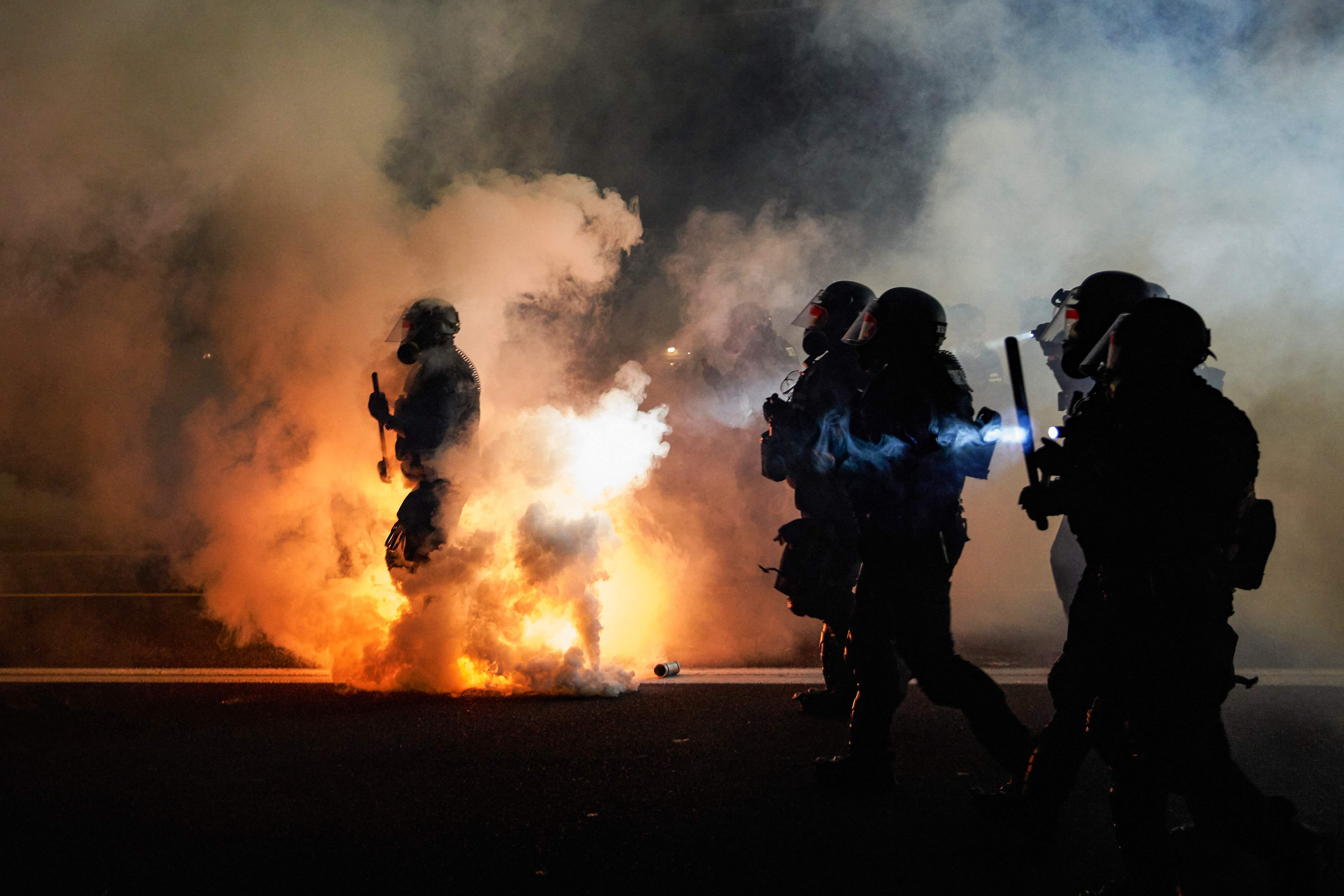 Oregon police wearing anti-riot gear march toward protesters through tear gas smoke during the 100th day and night of protests against racism and police brutality in Portland, Ore., on Sept. 5, 2020. Police arrested dozens of people and used tear gas against hundreds of demonstrators in Portland.