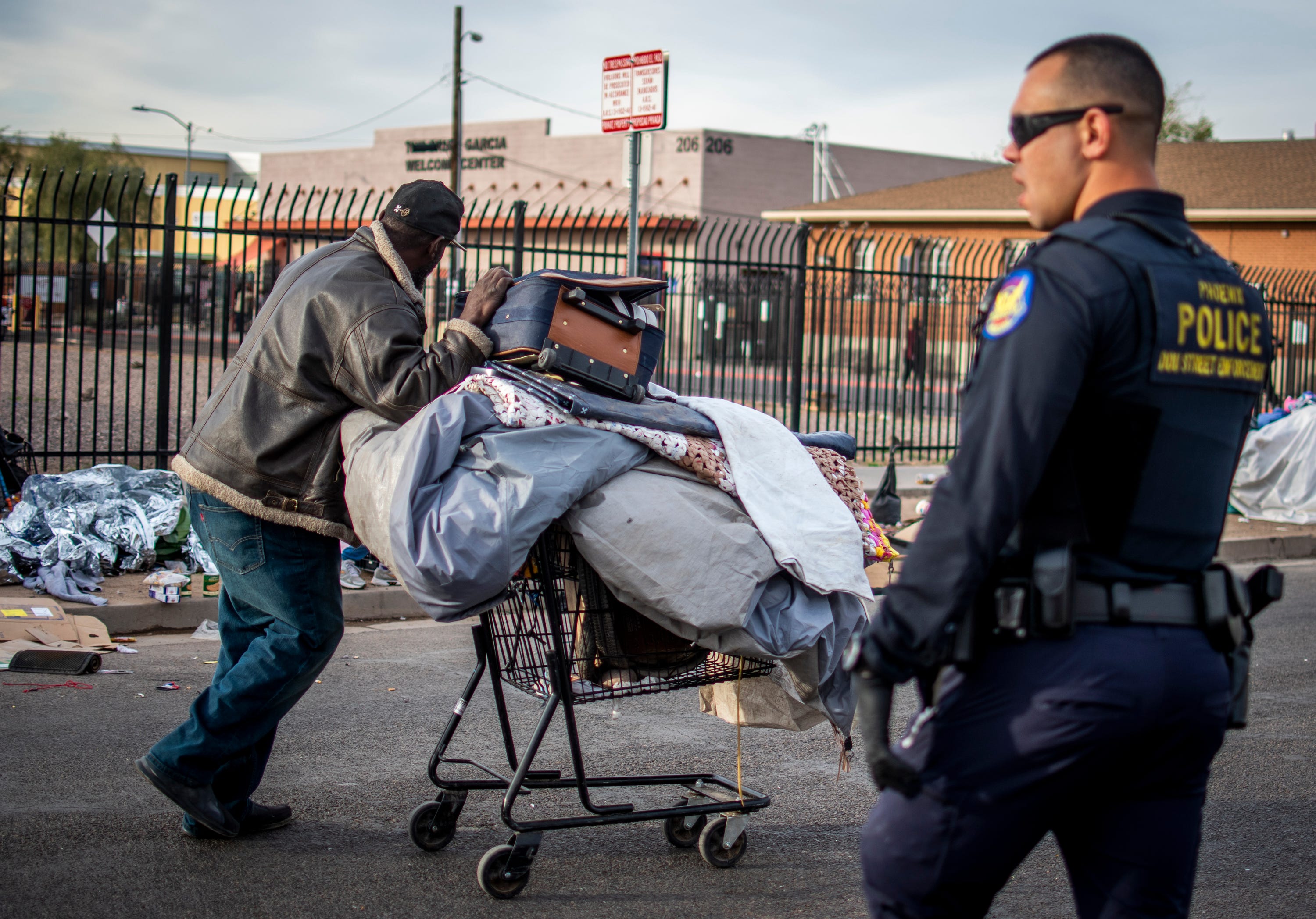 A man experiencing homelessness moves his belongings by a Phoenix police officer during an encampment removal on Feb. 5, 2020.