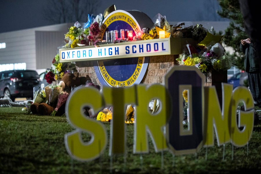 Community members leave candles, flowers and balloons at a memorial by the entrance of Oxford High School in Oxford on Wednesday, Dec. 1, 2021.