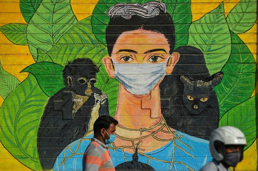 Pedestrians walk past a wall mural depicting Mexican painter Frida Kahlo wearing a face mask to spread awareness about the Covid-19 coronavirus in Mumbai on January 29, 2022.