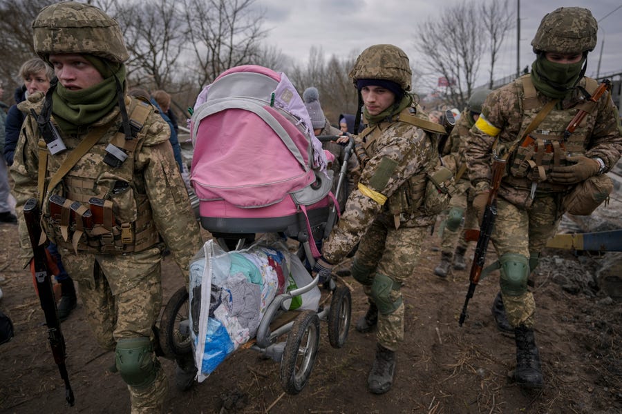 Ukrainian servicemen carry a baby stroller after crossing the Irpin River on an improvised path under a bridge that was destroyed by a Russian airstrike, while assisting people fleeing the town of Irpin, Ukraine, Saturday, March 5, 2022.