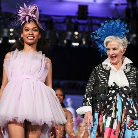 A model poses in a purple hat on the runway at the