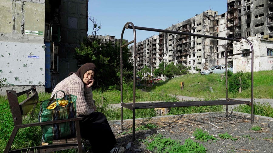 An elderly woman sits on a bench in a yard of destroyed residential buildings in Mariupol on May 31, 2022, amid the ongoing military action in Ukraine.