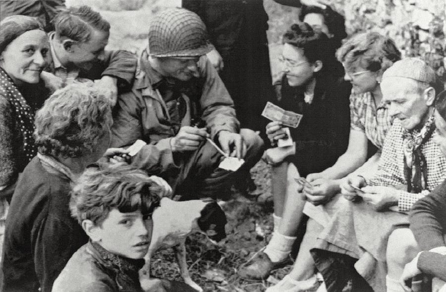 In this file photograph taken on June 6, 1944 Joseph Vaghi (C), a US Navy ensign, chats with residents of Colleville-Sur-Mer after Allied forces stormed the Normandy beaches during D-Day. - In what remains the biggest amphibious assault in history, some 156,000 Allied personnel landed in France on June 6, 1944. An estimated 10,000 Allied troops were left dead, wounded or missing, while Nazi Germany lost between 4,000 and 9,000 troops, and thousands of French civilians were killed. The 75th anniversary of the   D-day landings will fall on June 6, 2019.