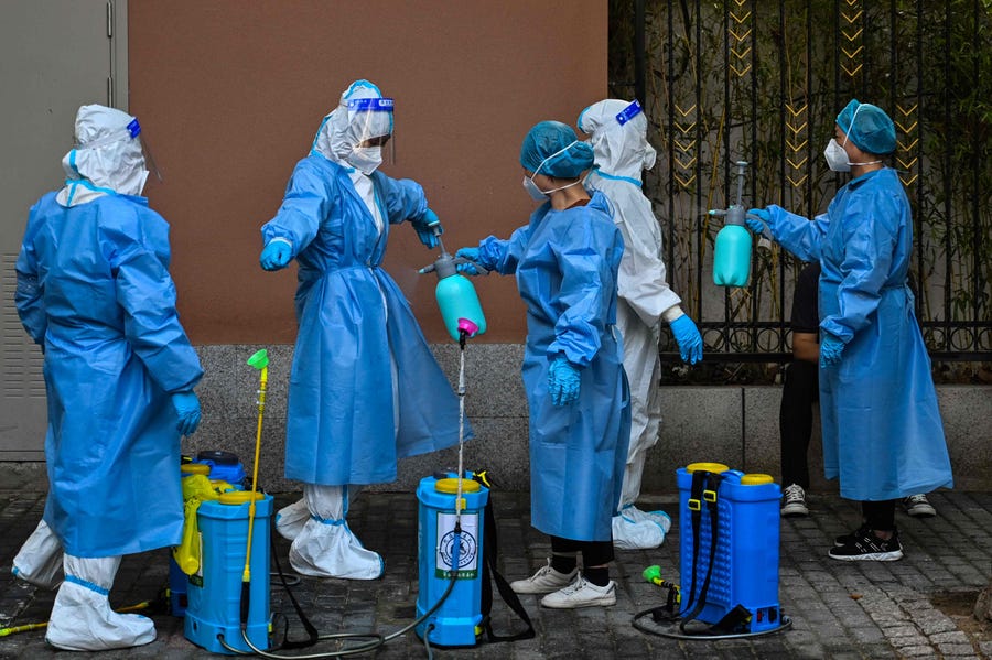 Workers spray disinfectant over colleagues in front of a residential area under a Covid-19 lockdown in the Huangpu district of Shanghai on June 4, 2022.