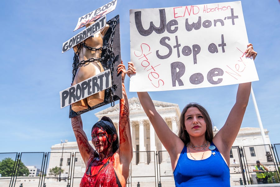 Abortion-rights supporter Sam Scarcello (L) and anti-abortion activist Elianna Geertgens hold competing signs in front of the Supreme Court while covered in fake blood on July 4, 2022 in Washington, DC. Protests continued across the country following the Supreme Courts decision overturning Roe v. Wade at the end of June.