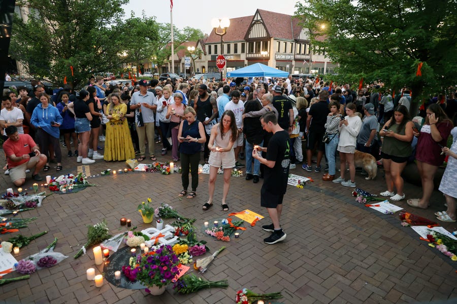 Dozens of mourners gather for a vigil near Central Avenue and St. Johns Avenue in downtown Highland Park, one day after a gunman killed at least seven people and wounded dozens more by firing an AR-15-style rifle from a rooftop onto a crowd attending Highland Park's Fourth of July parade, Tuesday, July 5, 2022 in Highland Park, Illinois.